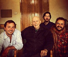 Photographie couleur de trois jeunes hommes entourant un vieux moine.