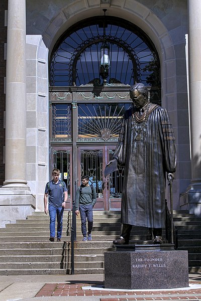 Two students walk out of Pogue Library near the statue of founder Rainey T. Wells.