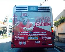 Een foto van een openbare bus van achteren, met een foto van een man met een rood shirt en hoed die poseert voor een advertentie tegen racisme