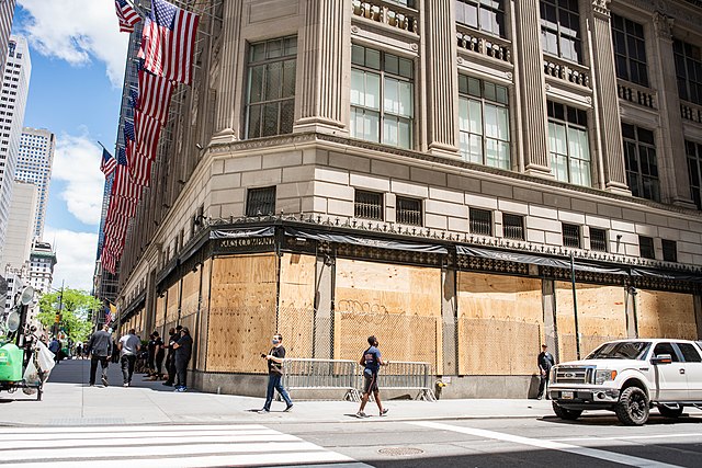 Private security guards, barbed wire fencing, and boarded up windows to prevent looting of department stores in New York City during mass unrest in th