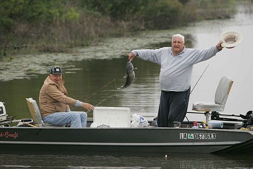 Two older men enjoying fishing from boat one man is standing and raising hat while showing the fish he just caught