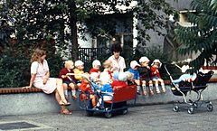 A group of East Berlin children, with their caretakers, 1984 East Berlin childminders, with children and strollers, seated on a wall, 1984.jpg