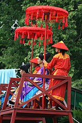Mandarins sitting uptop chairs while royal guards hold umbrellas.