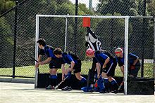 A group of five defenders, including the goalkeeper, prepare on the back line for a short corner. Fieldhockey shortcorner defense.jpg