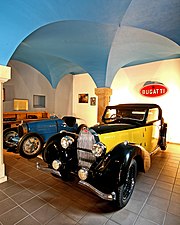 Photograph of a vaulted room containing two top-of-the-range cars from the inter-war period.