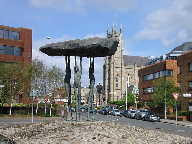 "Blackrock Dolmen" (1987) by Rowan Gillespie with the church St. John the Baptist in the background