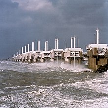 Een lange rij betonnen torens met stalen constructies die ze verbinden en een zeer ruwe zee