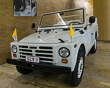 A white heavy-duty off-road vehicle with an open top. Two Vatican City flags are attached to the bonnet.