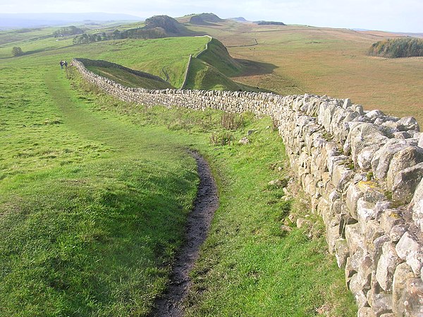 A view of Hadrian's Wall showing its length and height. The upright stones on top of it are modern, to deter people from walking on it.