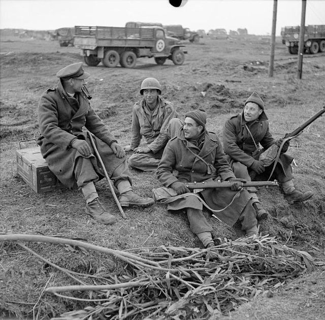 Reverend G. B. Fairhurst, Padre of the 2/5th Battalion, Queen's Royal Regiment, talking to two of the men in his battalion and an American soldier in 