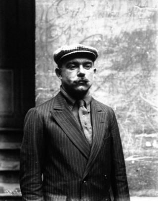 Portrait d'un homme vêtu d'un costume et d'une casquette, se tenant debout.