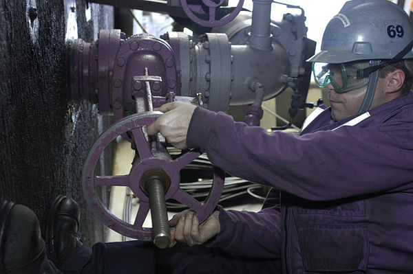 A sailor aboard a ship operates the wheel controlling a fuel valve.