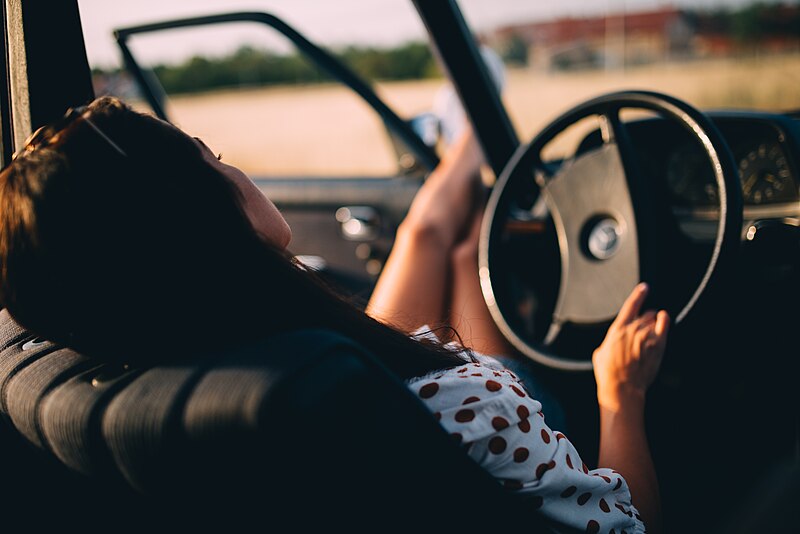 File:Woman holding a steering wheel and resting her legs on an open car door. (51634340455).jpg