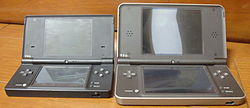 An opened clamshell dual-screen handheld device sits to the left of a larger version.