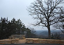 Inspiration Point in 2015, after major restoration efforts. Stone walls and a bench on grassy terrain overlooking the forested Root River Valley.