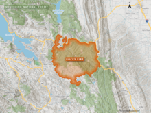 The Rocky Fire footprint is shown in bright orange as an irregular circle, bounded by CA 16 and CA 20 with Clear Lake to the west and Interstate 5 to the east