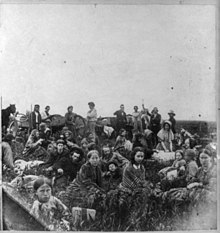 This photograph is titled "People escaping from the Indian massacre of 1862 in Minnesota, at dinner on a prairie". It is the right half of a stereograph published by Whitney's Gallery, St. Paul, Minn. This photo is actually "Mixed Bloods" who were rescued by non hostile Dakota. The girl in the foreground wrapped in the striped blanket is Elise Robertson, the sister of Thomas Robertson, a mixed blood who acted as an intermediary between the hostile and non hostile Dakota and the whites. Dakota War of 1862-stereo-right.jpg