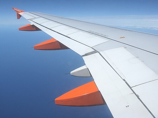 The three orange pods are fairings streamlining the flap track mechanisms. The flaps (two on each side, on the Airbus A319) lie directly above these.