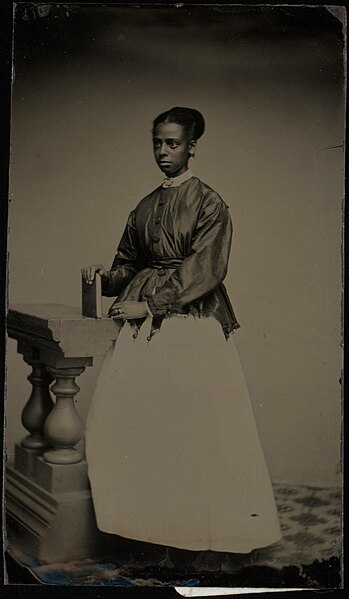 File:Full length portrait of young lady in white skirt, standing by baluster section. Tintype, ninth plate.jpg