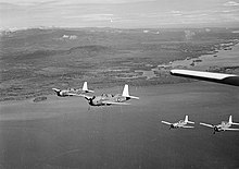 Sort / hvidt foto af fire enkeltmotorer, militære monoplaner, der flyver i formation nær en kystlinje