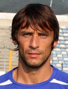 Cuello y rostro de hombre de frente.  Posa en un campo de fútbol, ​​tribuna al fondo.