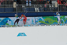 Photographie de trois hommes faisant du ski de fond, le premier en combinaison bleue, le second en rouge, le troisième en blanc, légèrement en retrait.