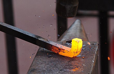 Rust scale forming and flaking off from a steel bar heated to its forging temperature of 1200°C. Rapid oxidation occurs when heated steel is exposed to air