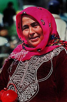Smiling woman outdoors wearing a brightly colored headscarf and embroidered clothing