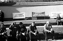 People sitting in front of banners in Lithuanian and Russian. The Russian one reads "The [economic] blockade - the new stage of real socialism"