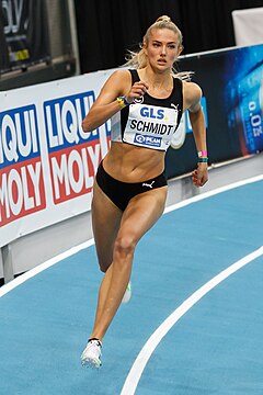 Blonde woman in a red top and black short running on a red track