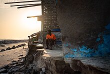 A man looking out over the beach from a building destroyed by high tides in Chorkor, a suburb of Accra. Sunny day flooding caused by sea level rise, increases coastal erosion that destroys housing, infrastructure and natural ecosystems. A number of communities in Coastal Ghana are already experiencing the changing tides. ANKOMAH 20221122-009.jpg