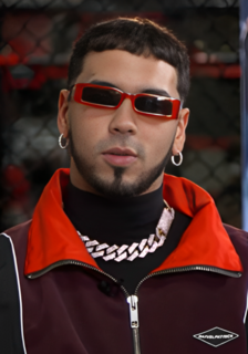 Emmanuel Gazmey Santiago, known professionally as Anuel AA, is a Puerto Rican rapper and singer. His music often contains samples and interpolations of songs that were popular during his youth. He is seen as a controversial figure in the Latin music scene for his legal troubles and feuds with fellow Puerto Rican rappers Cosculluela and Ivy Queen and with fellow American rapper 6ix9ine. Raised in Carolina, Puerto Rico, he started recording music at age fourteen and began posting it online four years later in 2010, before eventually signing to the Latin division of fellow American rapper Rick Ross's Maybach Music Group. His 2016 mixtape Real Hasta la Muerte was well-received, but his success was put on hold the same year by a 30-month prison sentence for illegal firearm possession in Puerto Rico. He recorded the entirety of his debut album while incarcerated, during which time his genre of music surged in popularity.