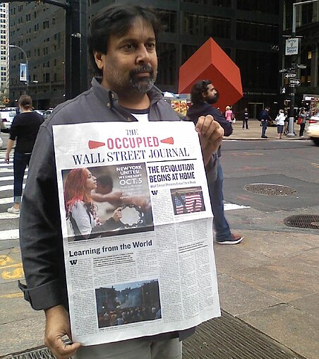 Arun Gupta, editor of Occupied Wall Street Journal holding a copy of the first issue, standing inside Zuccotti Park.