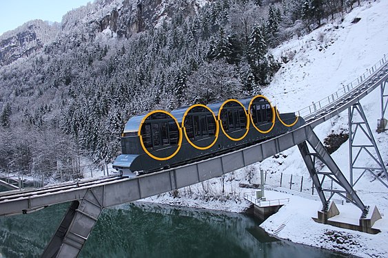 Neue Standseilbahn Schwyz–Stoos mit fast horizontal gelagerten Fahrgastkabinen noch unten im Tal im flachen Abschnitt über der Muota am Tag der Eröffnung (15. Dezember 2017)