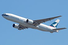 Front quarter view of the first 777 built in flight wearing Cathay Pacific livery and with flaps partially extended and landing gear retracted.