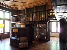 Fotografie color a unui dulap sub forma unui bufet jos în fața rafturilor din lemn sculptate ale unei biblioteci.
