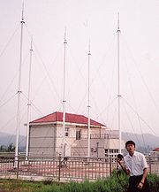 Homme posant devant cinq antennes blanches. Celles-ci sont soutenues par des câbles.
