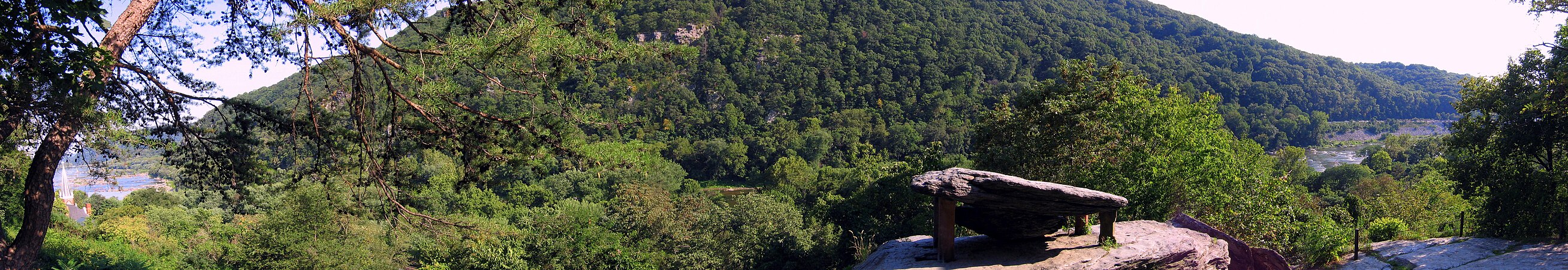 This is a panoramic view of Jefferson Rock (right foreground) and the surrounding river valley. The lower town of Harpers Ferry and the confluence of the Shenandoah and Potomac Rivers appears on the left. The church steeple (also left) belongs to St. Peter's Roman Catholic Church.