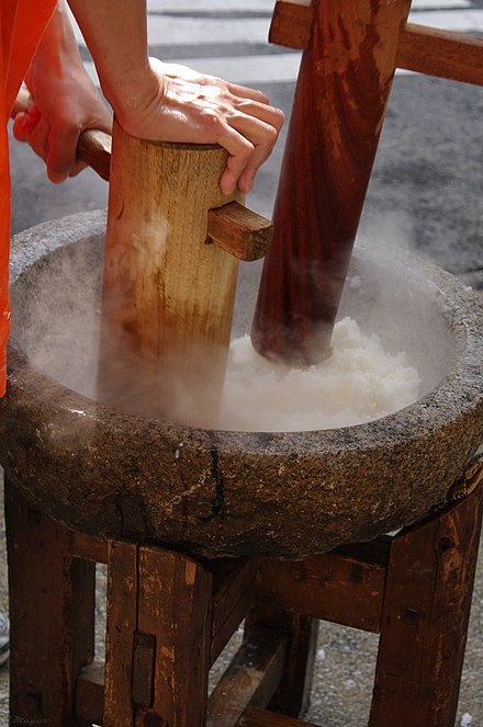 Steamed rice in a stone mortar being mashed with a wooden kine (pestle) during mochitsuki