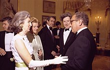 Photograph taken at a political reception in the 1970s; Vera Cosgrave and Henry Kissinger are in the foreground; in the background, Betty Ford, Henry Catto, and Garret FitzGerald.