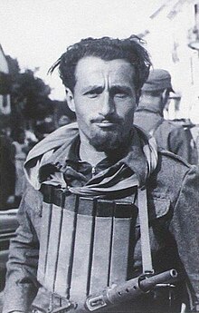 black-and-white photo of Pietro Chiodi wearing body armour and carrying a rifle, squinting at camera