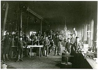 Maskinsalen med arbetsstyrkan år 1886. Färdiga ljusstakar och en stor ljuskrona i mässing.