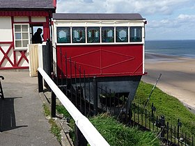 Cerbyd ar y brig yn aros i ddisgyn. Mae braciwr yn sefyll ar y chwith.