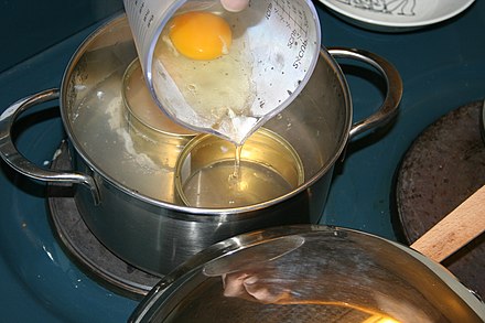 An egg being slowly poured into a ring mould in a pot of simmering water