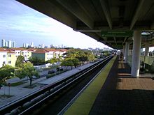 Quai de gare avec auvent et train en approche.