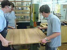 Students maneuver a large laminated board through a bandsaw together Band saw.JPG
