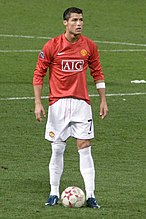 Cristiano Ronaldo – wearing long-sleeved red jersey, white shorts with a number 7 on the left-leg side and a white armband on the left arm – prepares to take a free kick.