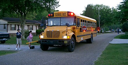 School bus at bus stop with 8-way warning lights, dual stop arms, and crossing arm