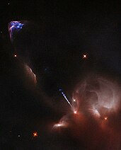 Images are in false colour. Bright yellow star in brown-appearing nebula shoots out a blue-white jet, which then causes blue and purple emissions from the surrounding medium upon impact.