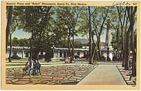 A linen postcard shows ten people variously sitting or walking in groups on the Plaza; old cars are parked in front of the Palace of the Governors' portal in the background